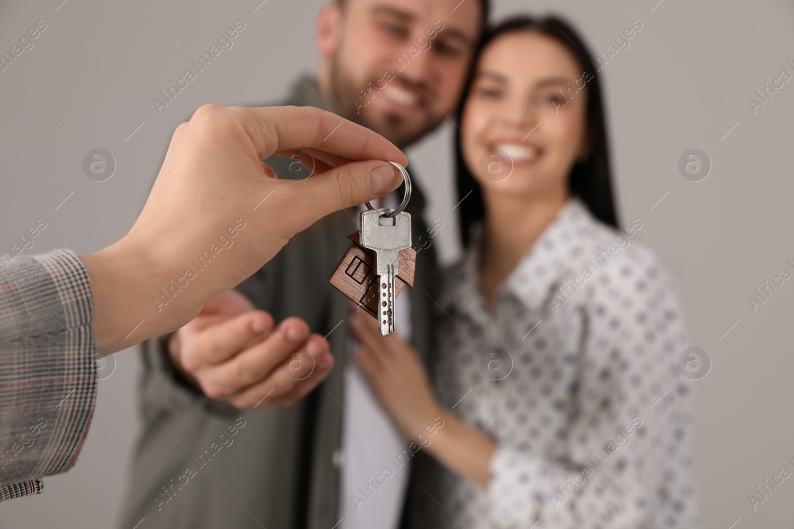 Photo of Real estate agent giving key to happy young couple against grey background, closeup