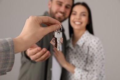 Photo of Real estate agent giving key to happy young couple against grey background, closeup