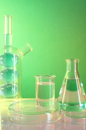 Laboratory analysis. Different glassware on table against green background, space for text