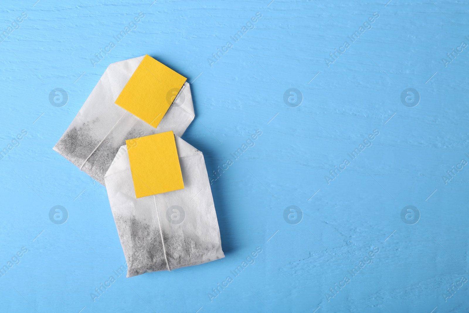 Photo of Tea bags with tabs on light blue wooden table, top view. Space for text