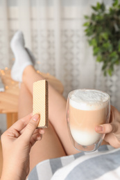 Woman having delicious wafer and coffee for breakfast indoors, closeup