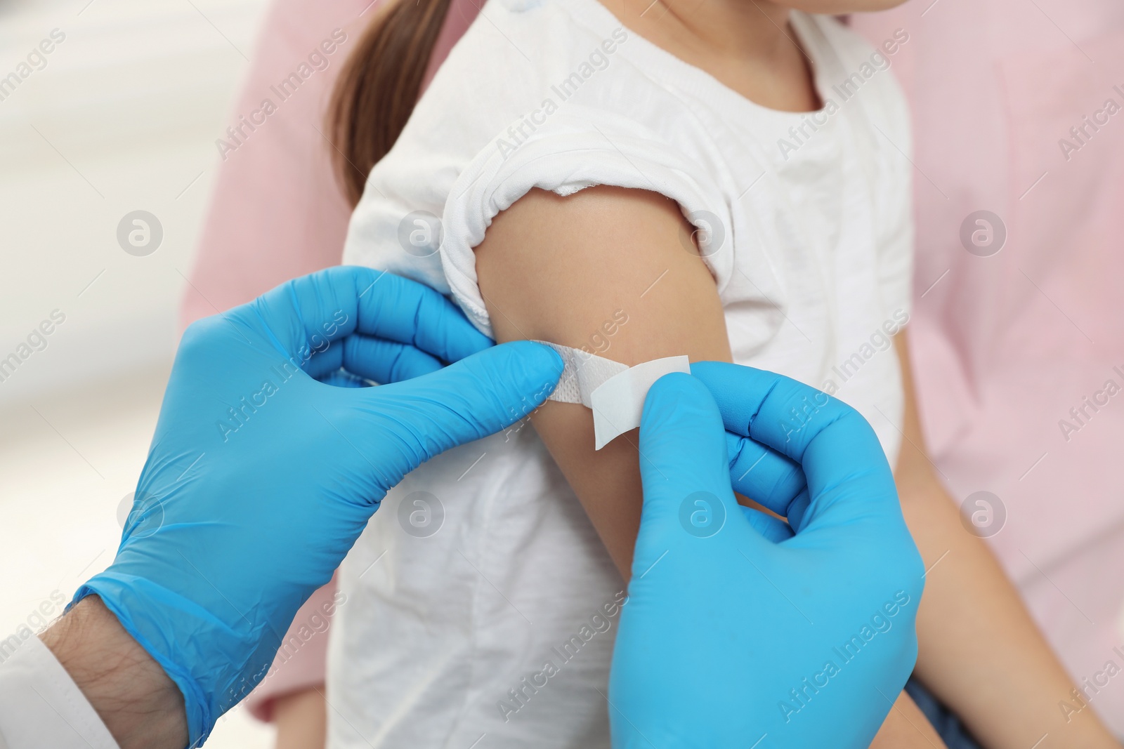 Photo of Children's hepatitis vaccination. Mother with her daughter. Doctor sticking medical plaster on little girl's arm, closeup