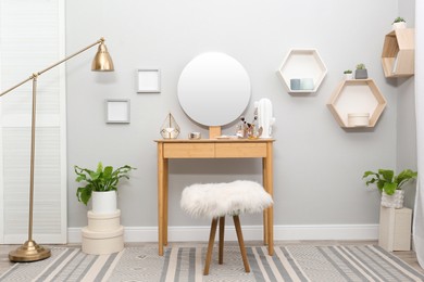 Stylish room interior with wooden dressing table and mirror on light wall
