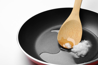 Frying pan with coconut oil and wooden spoon on white background, closeup. Healthy cooking