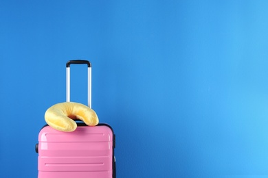 Photo of Pink suitcase and travel pillow on blue background, space for text