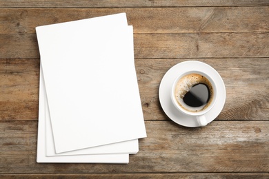 Blank paper sheets for brochure and cup of coffee on wooden background, flat lay. Mock up