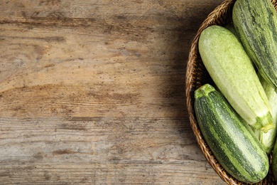 Wicker bowl with fresh ripe green zucchini on wooden background, top view. Space for text