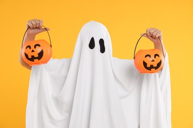 Woman in white ghost costume holding pumpkin buckets on yellow background. Halloween celebration