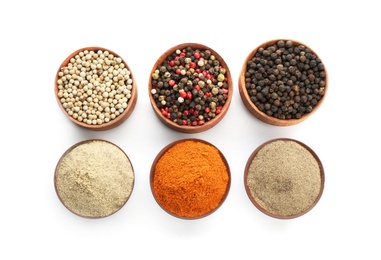 Bowls with different kinds of whole and milled pepper on white background, top view