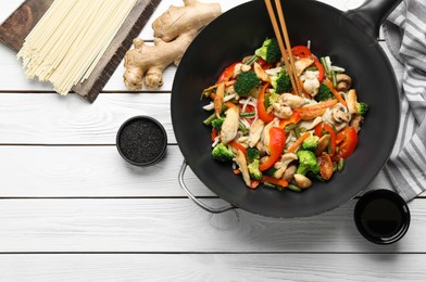 Photo of Stir fried noodles with mushrooms, chicken and vegetables in wok on white wooden table, flat lay