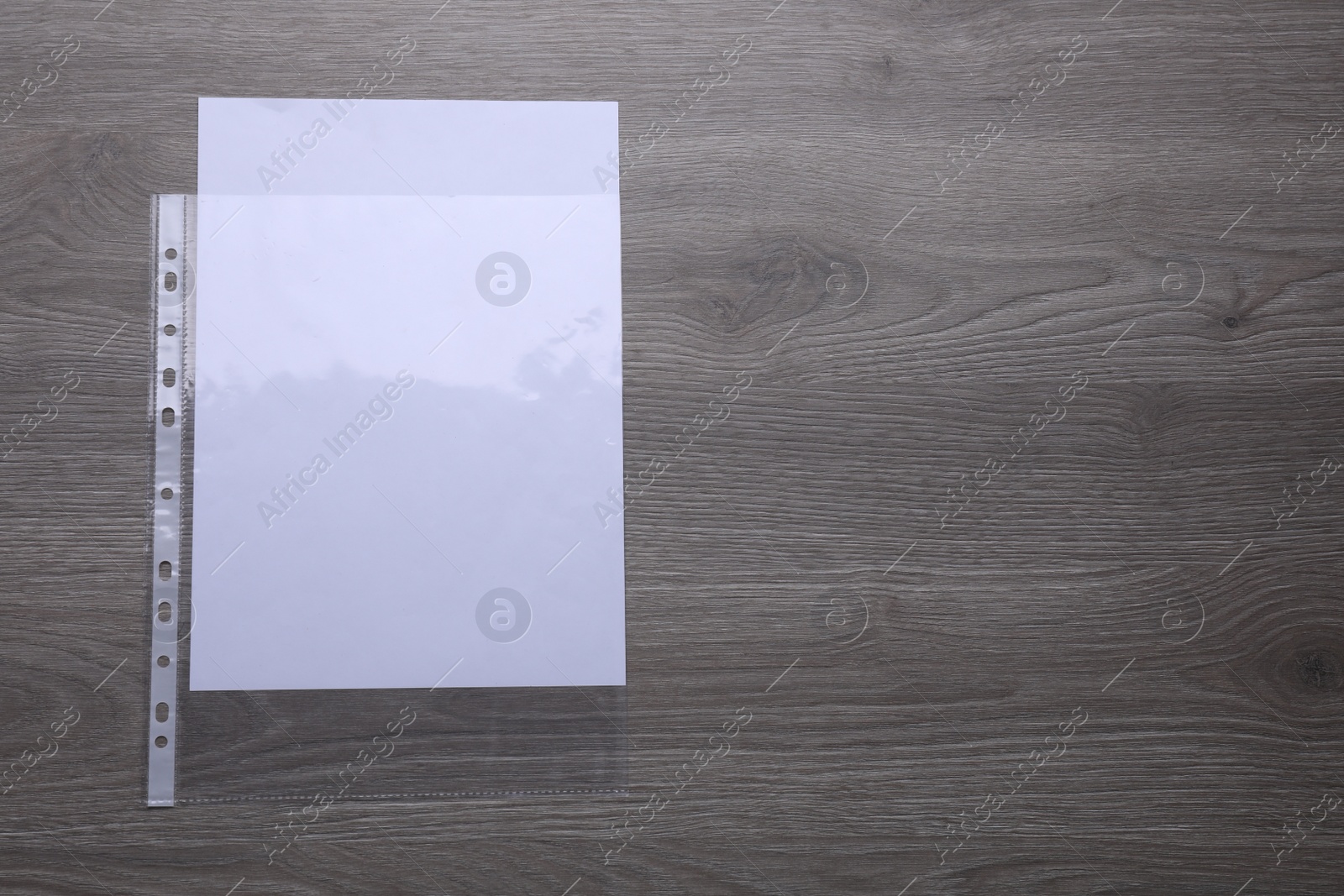 Photo of Punched pocket with paper sheet on wooden table, top view. Space for text