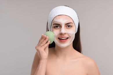 Photo of Young woman with headband washing her face using sponge on light grey background