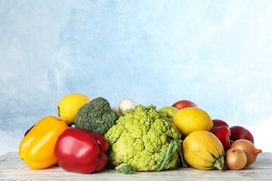 Variety of fresh delicious vegetables and fruits on table against color background