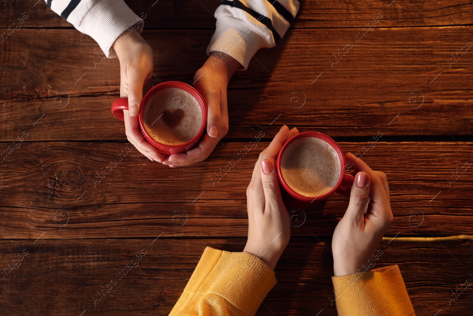 Photo of Women with mugs of hot coffee at wooden table, top view