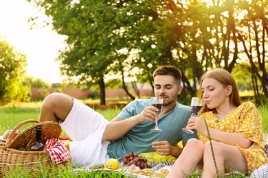 Photo of Happy young couple with glasses of wine having picnic outdoors