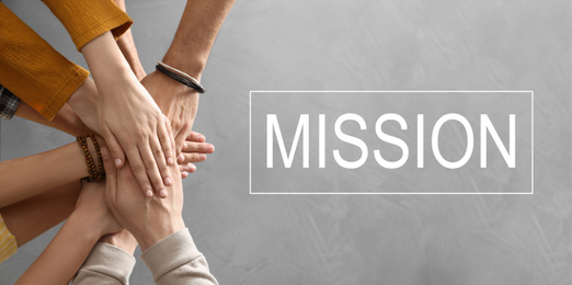 Image of People holding hands together over grey background and text MISSION, top view. Banner design