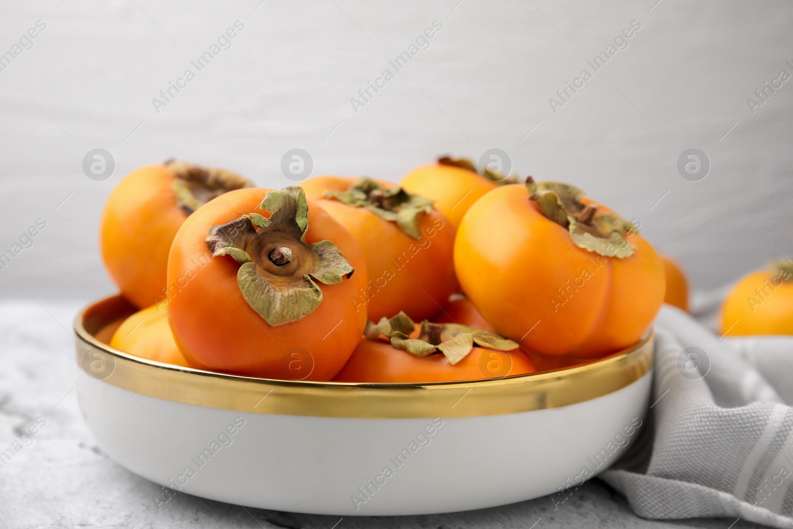 Photo of Bowl with delicious ripe juicy persimmons on table, closeup