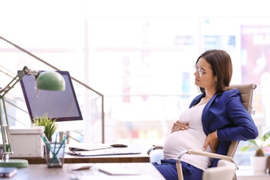 Photo of Young pregnant woman suffering from pain while working in office