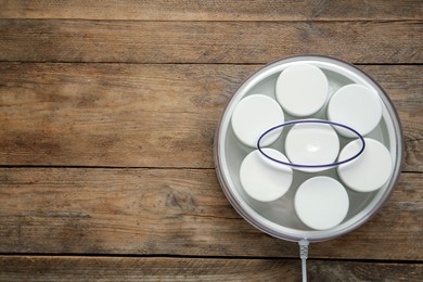 Modern yogurt maker with jars on wooden table, top view. Space for text