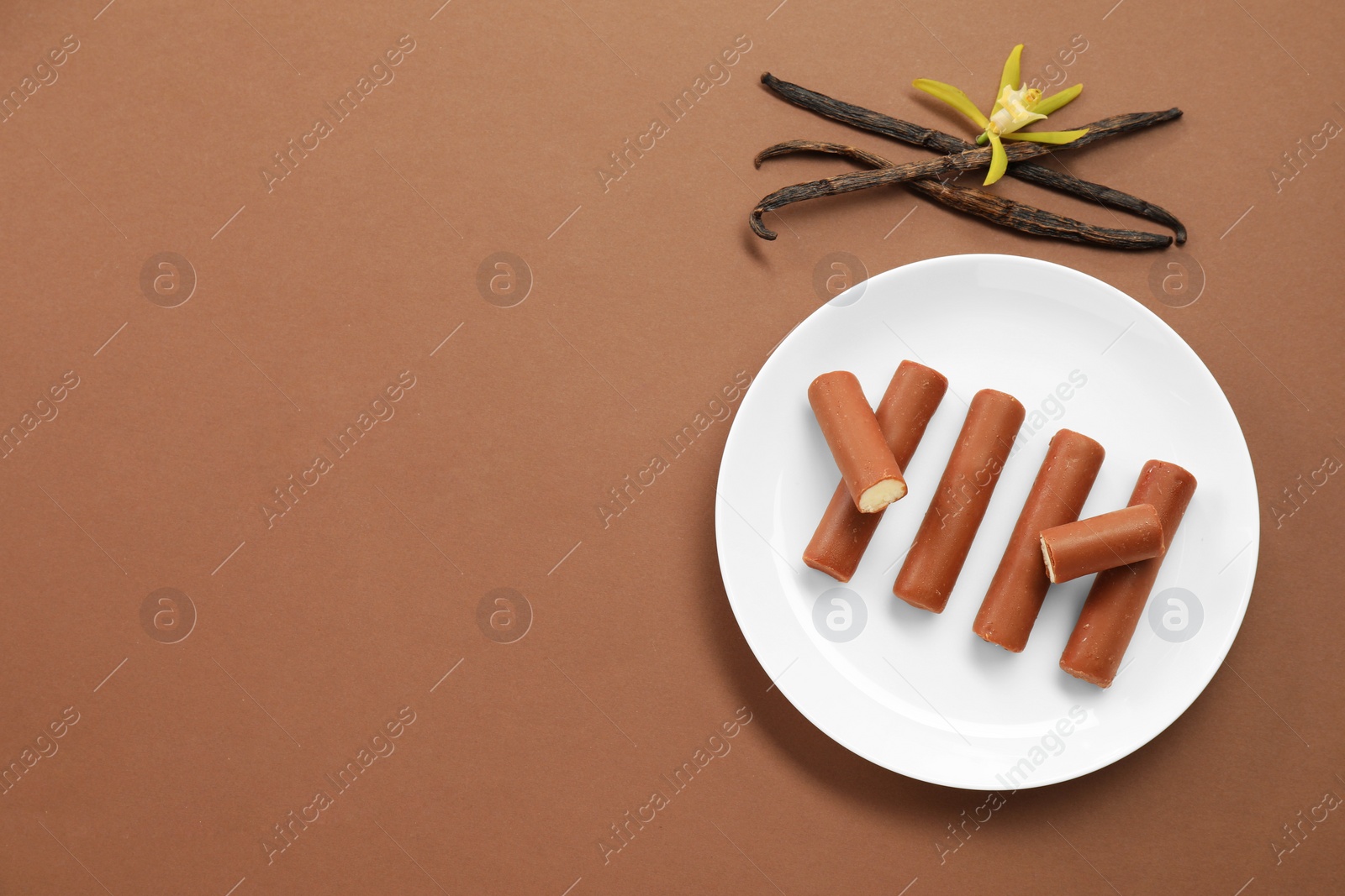 Photo of Glazed curd cheese bars, vanilla pods and flower on light brown background, top view. Space for text