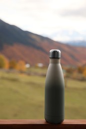 Thermo bottle on wooden surface in beautiful mountains