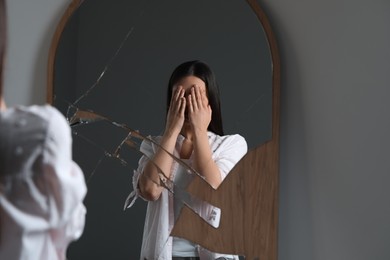 Young woman looking at herself in broken mirror indoors. Mental problems