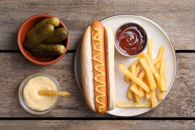 Photo of Flat lay composition with delicious hot dog and French fries on wooden table