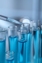 Dripping liquid from pipette into test tube in laboratory, closeup