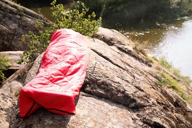 Photo of Man resting in sleeping bag on cliff near lake