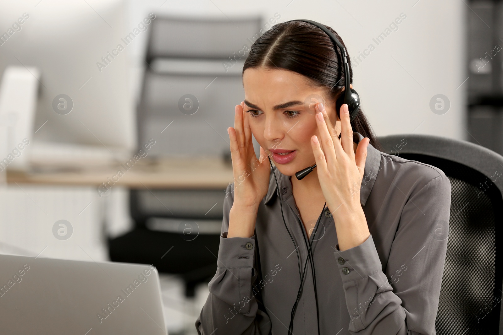 Photo of Stressed hotline operator with headset working on laptop in office