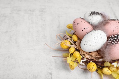 Photo of Decorative nest with many painted Easter eggs on light textured background, closeup. Space for text
