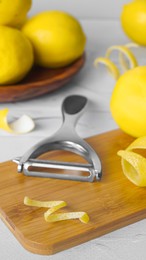 Photo of Wooden board, lemons, peeler and fresh rind on white textured table, closeup