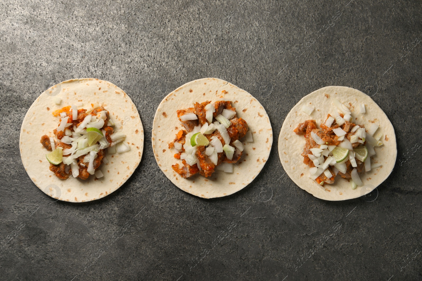Photo of Delicious tacos with vegetables, meat and lime on grey textured table, flat lay