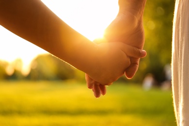 Photo of Little girl and her mother holding hands in park, closeup. Happy family