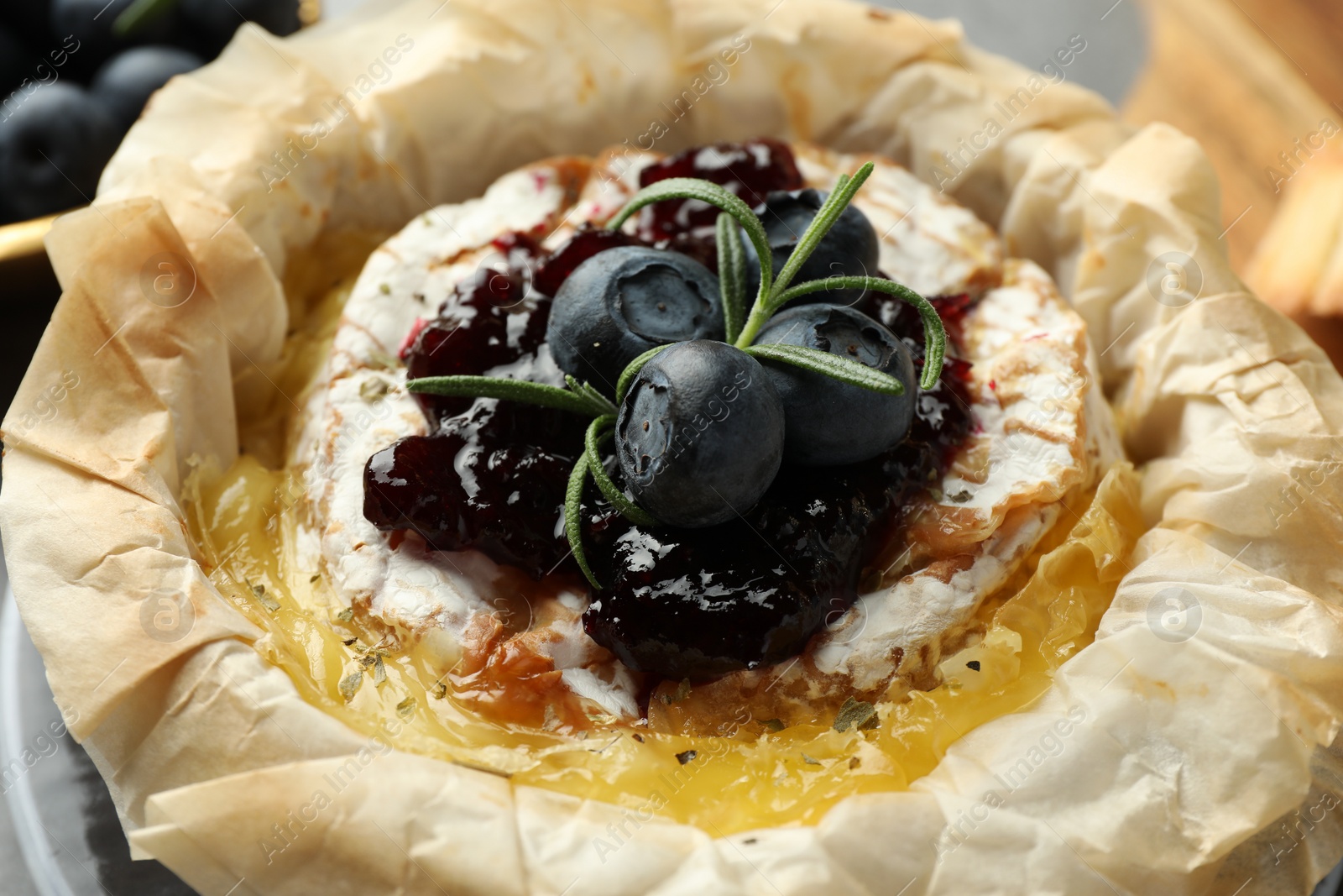 Photo of Tasty baked brie cheese with blueberries, jam and rosemary on table, closeup