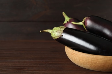 Photo of Ripe purple eggplants in bowl on wooden table, closeup. Space for text