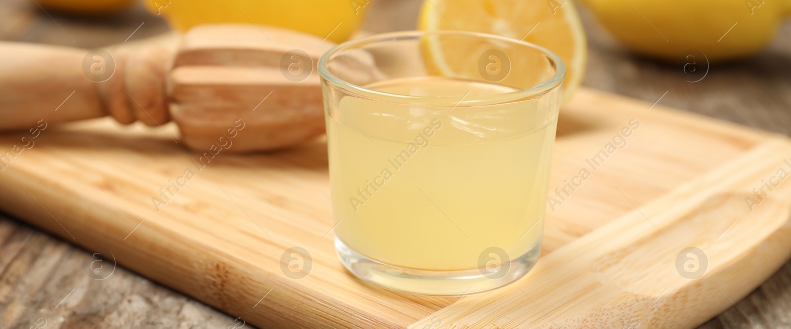 Image of Wooden board with glass of freshly squeezed lemon juice and reamer on table. Banner design