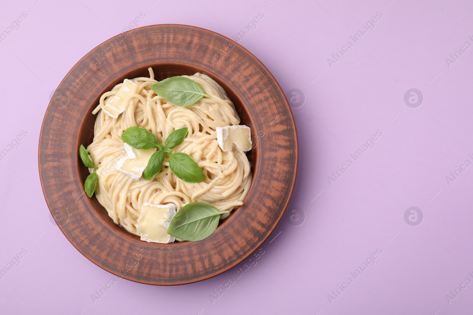 Photo of Delicious pasta with brie cheese and basil leaves on violet background, top view. Space for text