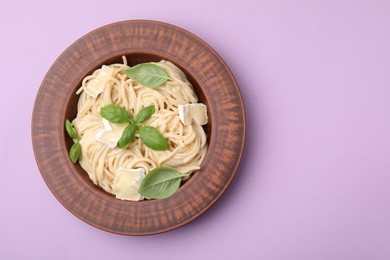 Delicious pasta with brie cheese and basil leaves on violet background, top view. Space for text