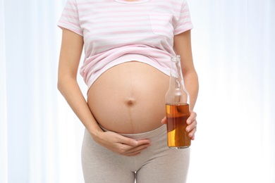 Photo of Pregnant woman with bottle of whiskey on light background. Alcohol addiction