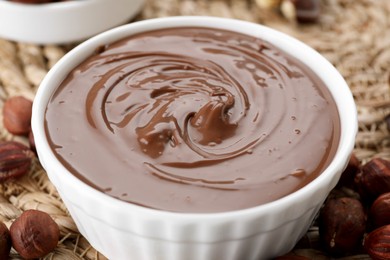 Photo of Bowl with tasty chocolate paste and nuts on wicker mat, closeup