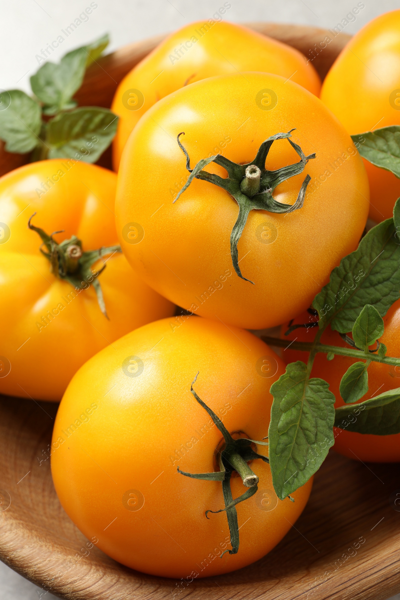 Photo of Fresh ripe yellow tomatoes with leaves in wooden bowl, closeup