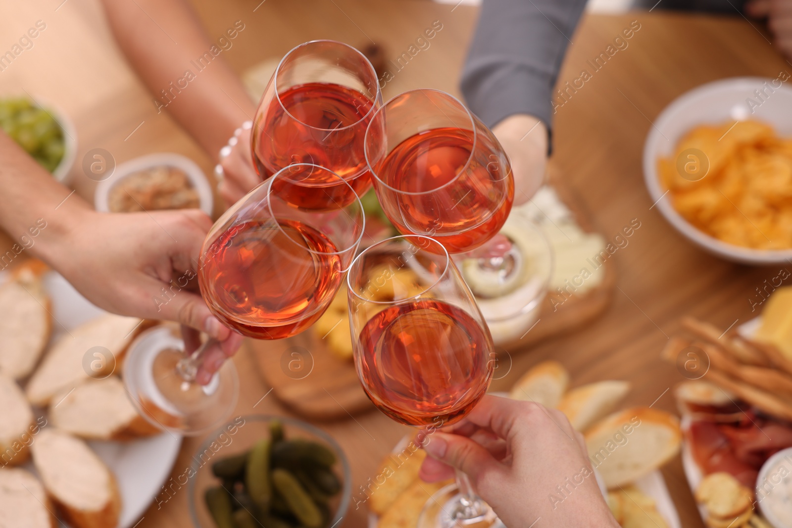 Photo of People clinking glasses with rose wine at wooden table, above view