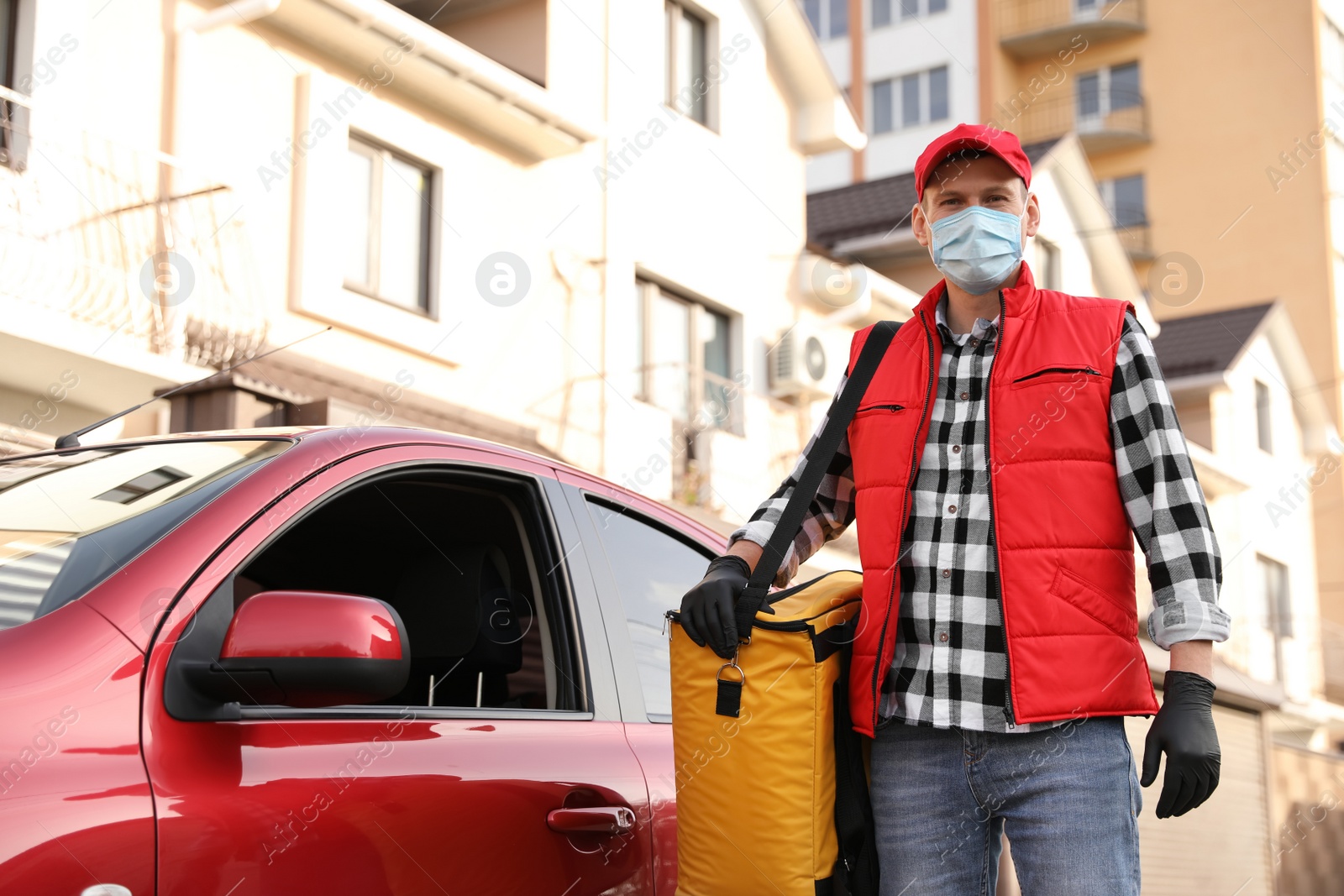 Photo of Courier in protective mask and gloves with thermobag near car outdoors. Food delivery service during coronavirus quarantine