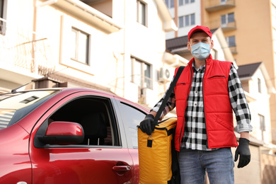 Courier in protective mask and gloves with thermobag near car outdoors. Food delivery service during coronavirus quarantine