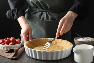 Shortcrust pastry. Woman making holes in raw dough with fork at grey table, closeup