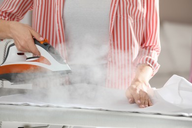 Photo of Young woman ironing clean laundry with steam, closeup