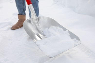 Woman removing snow with shovel outdoors, closeup