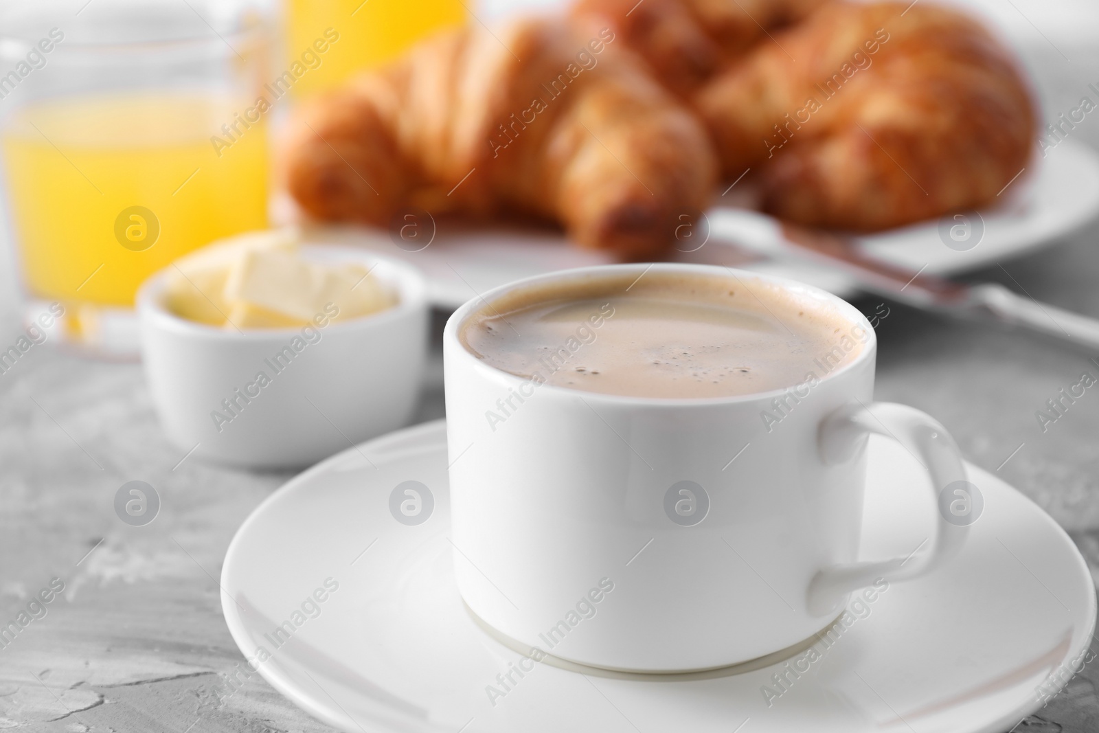 Photo of Tasty breakfast. Cup of coffee, butter and fresh croissants on grey table, closeup