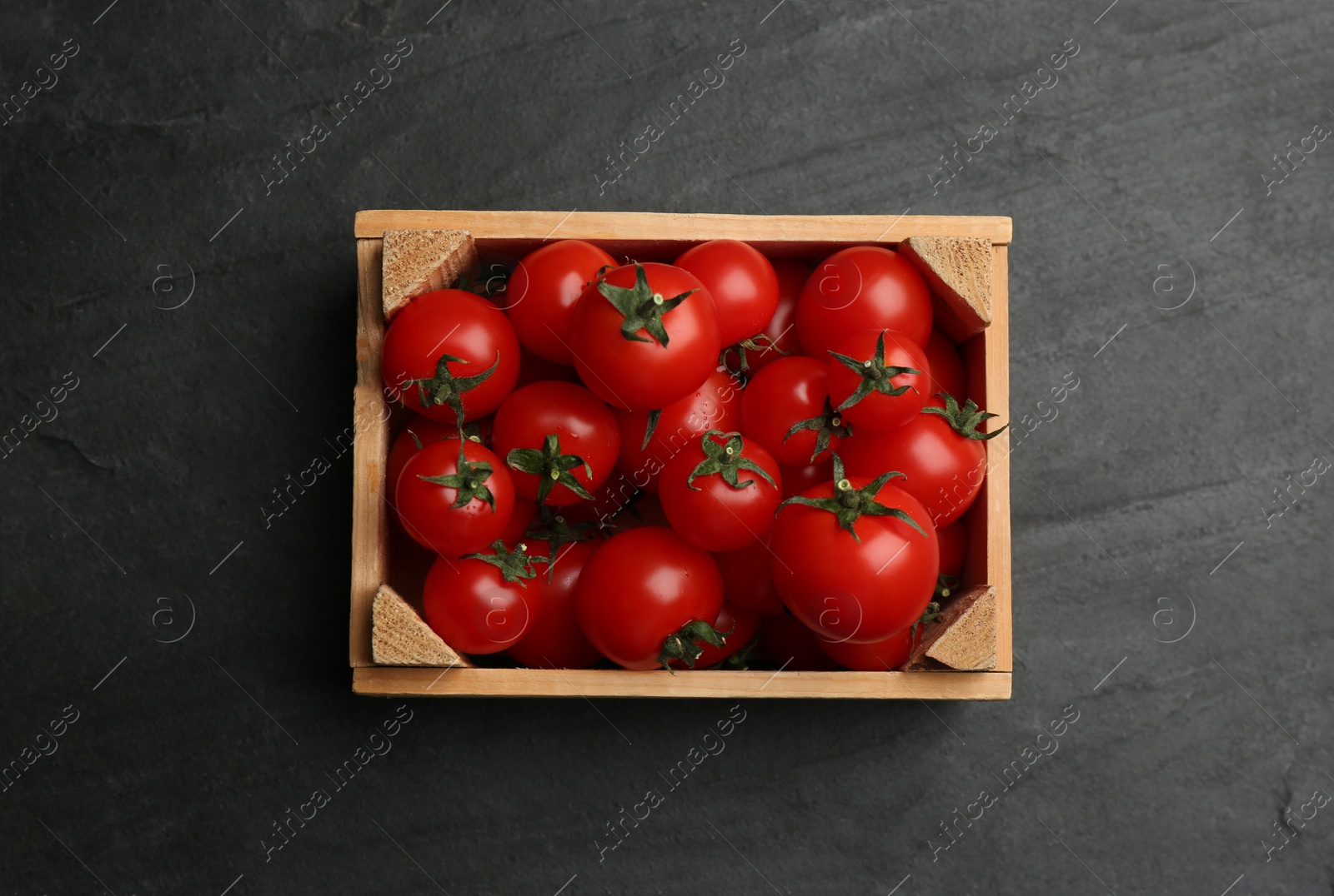 Photo of Fresh ripe cherry tomatoes in wooden crate on black table, top view